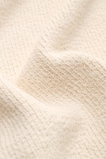 Nahaufnahme der weichen Bouclé-Struktur des 04651/ A trip in a bag Rundhalspullover 'Boucle Crew' beige, Detailfoto aus schräger Perspektive.