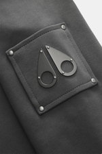 Nahaufnahme des Moose Knuckles Sweatshirts 'Hartsfield Crew' dunkelgrau, Fokus auf Metall-Logo-Patch am Oberarm, reine Baumwolle, weicher Griff, Rippbündchen.