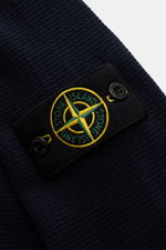 Close-up of the Stone Island Strickpolo navy sleeve, showing the finely textured pure cotton knit and the iconic compass badge on the upper arm, photographed from a side angle. Style trifft auf lässigen Komfort: Dieses Strickpolo überzeugt mit fein strukt