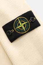 Close-up front view of the Stone Island Troyer pastellgelb showing the black compass badge with yellow and green embroidery on soft pastel yellow cotton knit fabric. <p>Vielseitiger Begleiter in der Übergangszeit: Der Troyer von STONE ISLAND wird mit sein