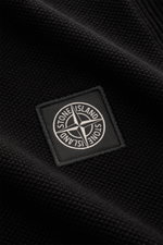 Nahaufnahme des Stone Island Kurzarm-Strickpolo schwarz mit feinem Piqué-Mix, Polokragen und STONE ISLAND-Weblabel frontal sichtbar.