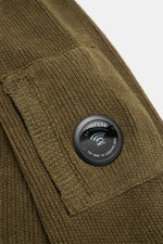 Nahaufnahme des Ärmels vom C.P. Company Strickpolo oliv aus schwerer Baumwoll-Chenille mit Label-Linsen-Detail, Tasche und mittelfeinem Strickbild.