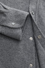 Nahaufnahme aus schräger Draufsicht des B.F. Knitwear Cashmere Strickhemd Kent-Kragen grau meliert mit weichem Griff, feinem Strickbild, Brusttasche, Druckknopfleiste und gerundetem Saum.