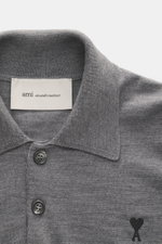 Nahaufnahme von Ami Paris Merino Strickpolo grau meliert aus reiner Merinowolle, weicher Griff, feines Strickbild, Regular Fit, typischer Polokragen, Drei-Knopf-Leiste, elastische Rippbündchen, Logo-Stitching auf der Brust, frontal fotografiert.