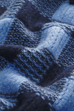 Nahaufnahme des Guest In Residence Strickpolo blau/navy kariert, fotografiert aus schräger Perspektive, zeigt mittelfeines Strickbild, Mix aus Wolle und Cashmere, weicher Griff, Regular Fit, Drei-Knopf-Leiste, gestrickter Polokragen und komfortable Rippbü