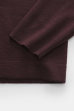 Nahaufnahme des Ärmels vom Kiefermann Merino Strickpolo 'Imano' bordeaux mit feinem Strickbild, weichem Griff, Oversized Fit, Polokragen und Drei-Knopf-Leiste, aus reine Merinowolle, von oben fotografiert.