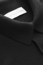 Kiefermann Merino Strickpolo 'Imano' schwarz, Detailaufnahme aus schräger Perspektive, reine Merinowolle, weicher Griff, feines Strickbild, Oversized Fit, typischer Polokragen, Drei-Knopf-Leiste.