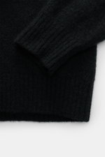 Nahaufnahme des Ärmels vom Filippo de Laurentiis Toyer schwarz, fotografiert von oben, zeigt mittelfeines Strickbild, flexible Rippbündchen, Oversized Fit, Troyer-Kragen, Mix aus Cashmere, Seide, Microfaser, sehr weicher Griff.