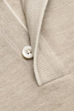 Nahaufnahme aus schräger Perspektive des beigen, melierten Moorer Cashmere Feinstrickpolo 'Teramo' mit feinem Strickbild, Perlmuttknopf und schmalen Kontrastkanten, gefertigt aus weichem Baby Cashmere.
