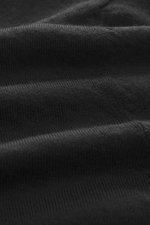 Close-up, angled view of the black fabric texture of the B.F. Knitwear Merino knit polo black, knit from pure merino wool with a soft feel, fine knit pattern, regular fit, classic polo collar, and flexible ribbed cuffs.