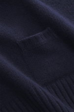 Nahaufnahme des feinen Strickbilds und der kleinen eingestrickten Tasche des 04651/ A trip in a bag Strickpolo navy aus Merinowolle und Cashmere, fotografiert aus seitlicher Perspektive.