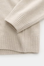 Nahaufnahme des Ärmels und Saums des 04651/ A trip in a bag Strickpolo sand, feines Strickbild aus Merinowolle und Cashmere, weicher Griff, Rippstrickbündchen und seitliche Details sichtbar.