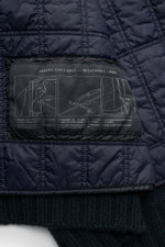 Nahaufnahme des herausnehmbaren Innenfutters der Stone Island Cashmere Strickjacke 'Ghost Piece' navy aus der Ghost-Kollektion, zeigt navyblaues, windabweisendes Material mit Anleitungsetikett, fotografiert aus Vogelperspektive. Vielseitiges Essential: re