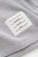 Nahaufnahme des Thom Browne Cardigan hellgrau meliert aus fein strukturierter Baumwolle mit markentypischem Weblabel, fotografiert von oben.