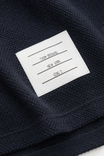 Nahaufnahme des Thom Browne Cardigan navy aus fein strukturierter, reiner Baumwolle mit markantem Weblabel, fotografiert von oben.