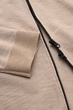Nahaufnahme der Stone Island Sweatjacke beige im Linksstrick, Fokus auf Reißverschluss, Rippstrickbündchen und geteilte Kängurutasche.