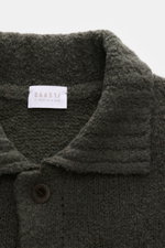 Nahaufnahme aus schräger Perspektive des olivfarbenen 04651/ A trip in a bag Cardigan 'Chunky Overshirt' mit voluminösem Strickbild, Umlegekragen und Knopf.