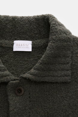 Nahaufnahme aus schräger Perspektive des olivfarbenen 04651/ A trip in a bag Cardigan 'Chunky Overshirt' mit voluminösem Strickbild, Umlegekragen und Knopf.