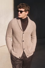Side-front view of a man wearing a slim fit von Braun Cashmere cardigan beige in chunky brioche stitch with shawl collar and four-button placket.