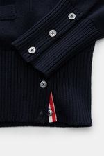 Nahaufnahme des Thom Browne Cardigan navy von schräg oben, reine Baumwolle mit mittelfeinem Strickbild, Knöpfe, V-Ausschnitt, Leistentaschen und rotem Kontraststreifen innen.