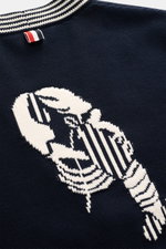 Nahaufnahme des Thom Browne Cardigan navy aus reiner Baumwolle mit mittelfeinem Strickbild, Rückmotiv, Weblabel und kontrastierendem Kragen, von oben fotografiert.