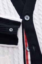 Nahaufnahme des Thom Browne Cardigan weiß/schwarz, fotografiert von oben, zeigt Zopfstrick aus reiner Schurwolle mit weichem Griff, Slim Fit, Vier-Knopf-Leiste und kontrastfarbenen Streifen am Arm.