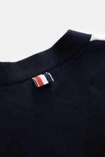 Nahaufnahme des Thom Browne Cardigans weiß/schwarz mit klassischem Zopfstrick, weichem Griff und kontrastfarbenem Streifen am Arm, fotografiert von oben.