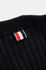 Nahaufnahme des Thom Browne Cardigan navy, schräg von oben fotografiert, zeigt Rippstrick, weiche Wolle und markante Streifen am Bund.