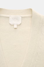 Nahaufnahme des cremefarbenen A.P.C. Cardigan 'Kevin' aus reiner Wolle mit Rundhalsausschnitt, Rippbündchen und Logoetikett, frontale Perspektive.