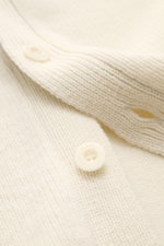 Nahaufnahme des A.P.C. Cardigan 'Kevin' creme aus reiner Wolle, Fokus auf Rippbündchen, Knöpfe und leicht griffige Haptik aus schräger Perspektive.