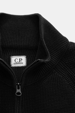 Nahaufnahme der C.P. Company Strickjacke schwarz aus mittlerer Perspektive, puristisches Design mit Waffelstrick, Baumwolle und Microfaser, Slim Fit, Stehkragen, robuster Zwei-Wege-Reißverschluss.