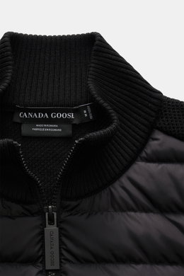 Nahaufnahme aus schräger Perspektive der Canada Goose Strickjacke 'Hybridge Knit' schwarz mit hochschließendem Stehkragen aus reiner Wolle und Daunen-Front, robuster Reißverschluss sichtbar.