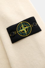Stone Island Strickjacke 'Lambswool' creme Nahaufnahme des Kompass-Badges auf wärmendem Wollmix mit Linksstrick und Filzdetails, frontale Perspektive.