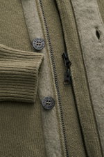 Close-up front view of Stone Island Cardigan 'Lambswool' olive showing knit wool blend, embossed buttons, felt details, two-way zip, and ribbed cuff, a stylish essential for cool days with distinctive purl-knit sections and signature compass badge.
