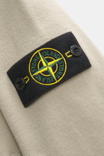 Nahaufnahme der Stone Island Strickjacke 'Stretchwool' sand mit Kompass-Badge am Ärmel, Detailansicht des fein gestrickten Wollmix-Stoffs.