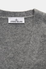 Nahaufnahme aus schräger Draufsicht des Stone Island Cardigan grau meliert mit weichem Griff, mittelfeinem Strickbild, V-Ausschnitt, Vier-Knopf-Leiste, Rippbündchen, Kompass-Badge, aus Alpaka, Schurwolle und Microfaser, Oversized Fit.