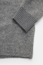Nahaufnahme des Stone Island Cardigan grau meliert, Perspektive auf das Ärmelbündchen mit mittelfeinem Strickbild, weichem Griff, Rippbündchen, Materialmix aus Alpaka, Schurwolle und Microfaser.