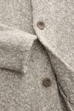 Nahaufnahme aus seitlicher Perspektive des 04651/ A trip in a bag Cardigan grau/offwhite meliert mit voluminösem Strickbild, weichem Griff und Knöpfen.