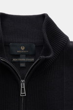 Close-up front view of Belstaff Cardigan 'Commander' black showing ribbed stand-up collar, concealed metal zipper, pure cotton with slightly textured quality, fine rib stitch pattern, flat knit details, slim fit, BELSTAFF woven label on upper arm, and fle