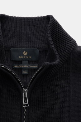 Close-up front view of Belstaff Cardigan 'Commander' black showing ribbed stand-up collar, concealed metal zipper, pure cotton with slightly textured quality, fine rib stitch pattern, flat knit details, slim fit, BELSTAFF woven label on upper arm, and fle