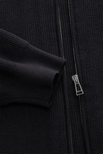 Close-up front view of Belstaff Cardigan 'Commander' black showing pure cotton fabric with slightly textured quality, fine rib stitch pattern, flat knit details, slim fit, concealed metal zipper, ribbed stand-up collar, BELSTAFF woven label on upper arm, 