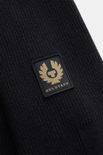 Close-up view of the Belstaff Cardigan 'Commander' black showing the pure cotton fine rib stitch pattern, slightly textured quality, and BELSTAFF woven label on the upper arm.