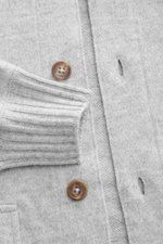 Nahaufnahme des Fioroni Cashmere Cardigan hellgrau meliert aus reiner Cashmere, zeigt weichen Griff, feines Strickbild, Knopf- und Knopflochdetails, Rippbündchen und aufgesetzte Taschen, fotografiert aus seitlicher Perspektive.