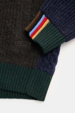 Nahaufnahme der Barbour Strickjacke 'Gamefair' multicolor mit grobem Zopf- und Patentstrick, grünem Rippbündchen und Paul-Smith-Streifen am Ärmelbündchen, fotografiert von oben.