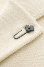 Nahaufnahme des Lardini Cashmere Strickblazers creme mit feinem Strickbild und schwarzem Blüten-Anstecker auf fallendem Revers, Detailansicht.