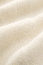Lardini Cashmere Strickblazer creme im Slim Fit, frontale Nahaufnahme zeigt feines, glattes Strickbild mit Blüten-Anstecker am fallenden Revers.