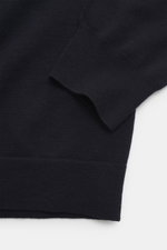 Nahaufnahme der C.P. Company Strickjacke navy im Detail, Perspektive auf Ärmelbündchen mit feinem Strickbild, Schurwolle-Microfaser, Regular Fit, Zwei-Wege-Reißverschluss, Stehkragen, Oberarmtasche und Linsen-Detail.