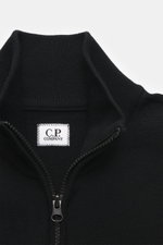 Nahaufnahme der C.P. Company Strickjacke schwarz von oben, Regular Fit aus Schurwolle und Microfaser, feines Strickbild, robuster Zwei-Wege-Reißverschluss, hochschließender Stehkragen, aufgesetzte Tasche am Oberarm, labeltypisches Linsen-Detail.