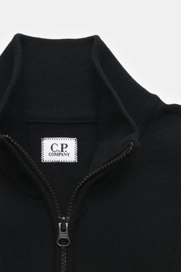 Nahaufnahme der C.P. Company Strickjacke schwarz von oben, Regular Fit aus Schurwolle und Microfaser, feines Strickbild, robuster Zwei-Wege-Reißverschluss, hochschließender Stehkragen, aufgesetzte Tasche am Oberarm, labeltypisches Linsen-Detail.