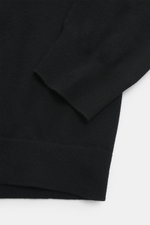 Nahaufnahme der C.P. Company Strickjacke schwarz von oben mit feinem Strickbild, Regular Fit, Stehkragen, Zwei-Wege-Reißverschluss, Oberarmtasche, Linsen-Detail, Schurwolle und Microfaser.